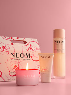 NEOM home and bath & body products including a candle, bath foam, and gift set box on a pink background