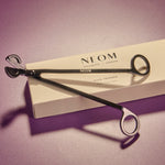 NEOM wick trimmer on a purple background with packaging