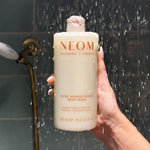 NEOM super shower power body wash in the shower being held by a person