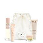 NEOM Sweet Dreams Travel Kit including a pillow mist, sleep pen, wonder balm and body butter with a white drawstring bag on a white background.