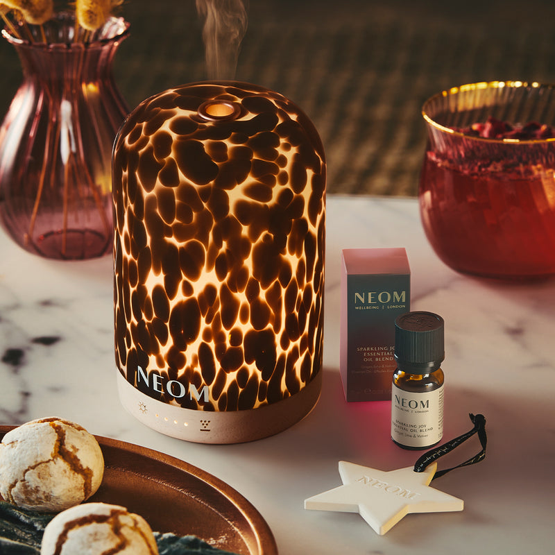 NEOM Tortoiseshell pod diffuser on a table with a NEOM essential oil blend and decorative items.
