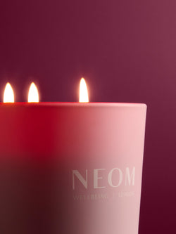 NEOM candle with three lit wicks on a dark background