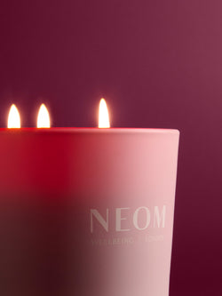 NEOM candle with three lit wicks on a dark background
