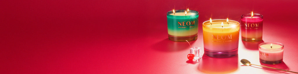 Set of colourful christmas candles with 'NEOM' branding on a red background